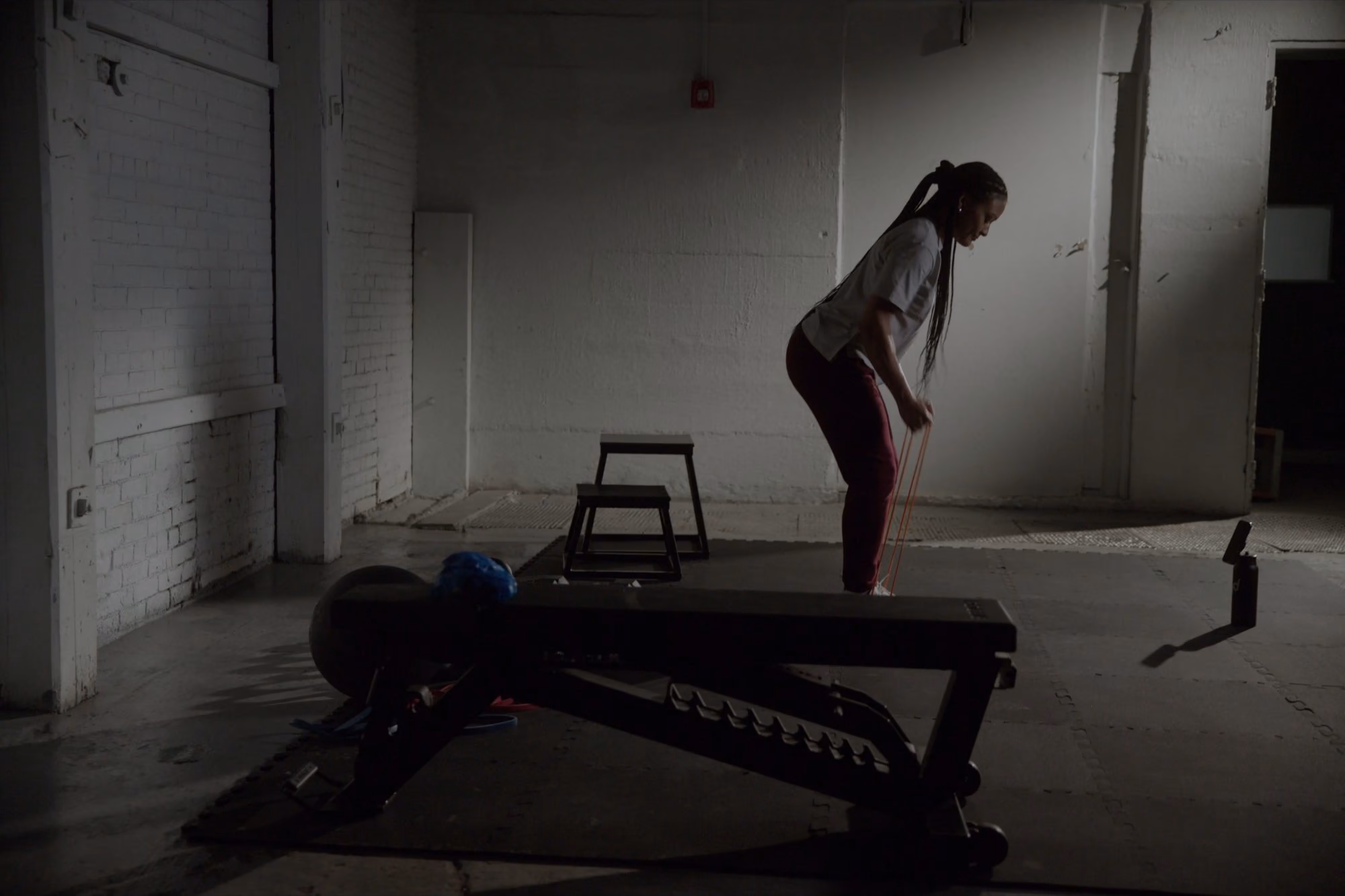 A woman pulls a resistance band in an empty warehouse gym.