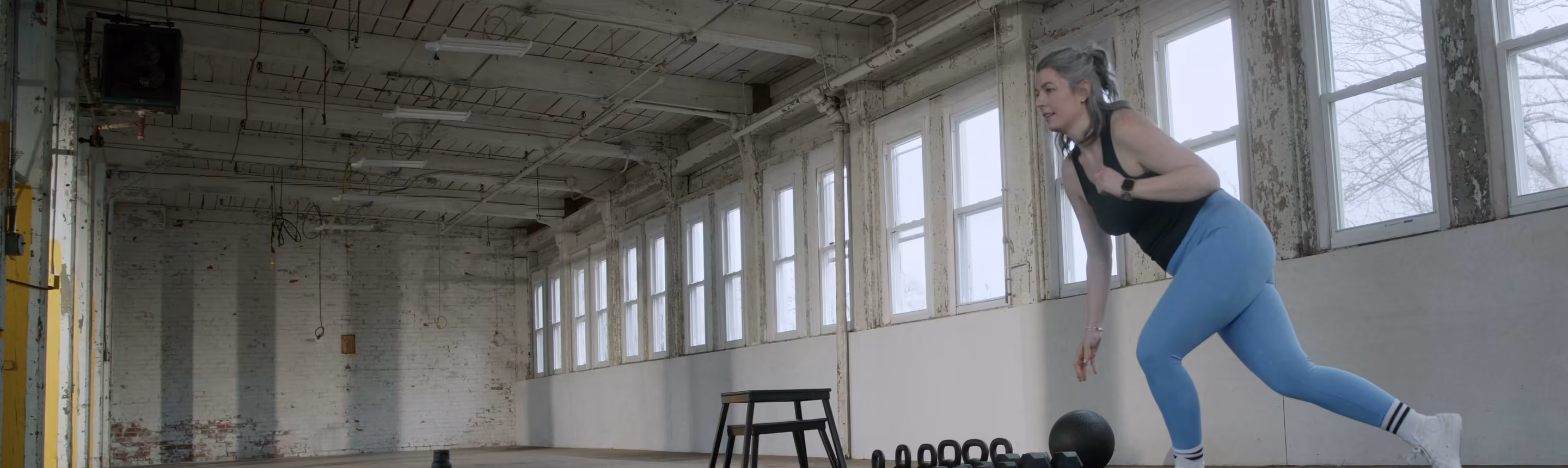 A woman lunges across a wide, sunlit gym floor