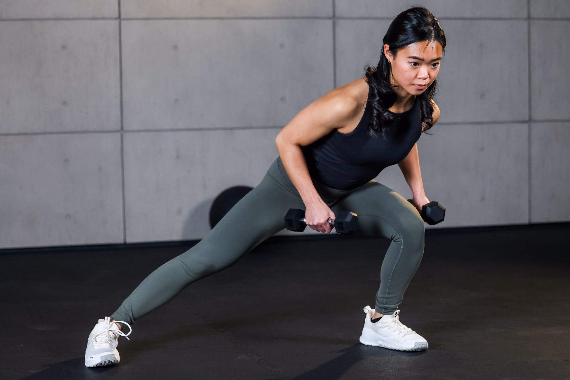 A woman lunges to the side with a dumbbell in each hand.