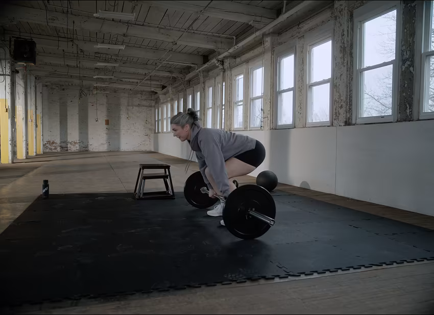 A woman lifts a loaded barbell from the floor of an industrial gym