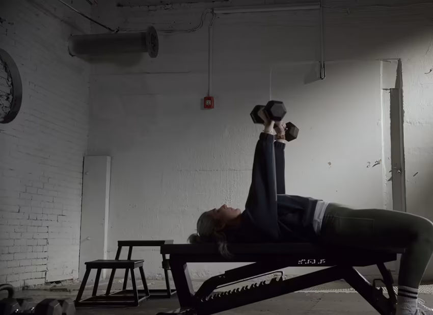 A woman presses dumbbells while lying on a bench