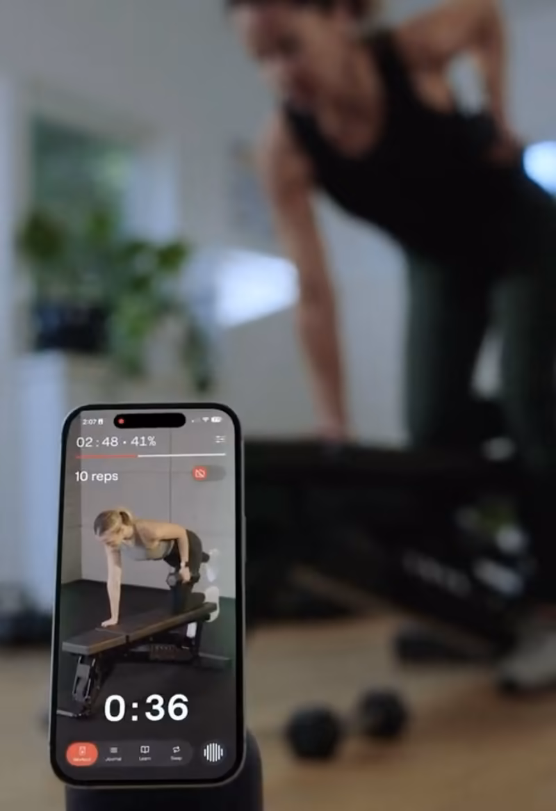 A phone on the floor counts down a set while a woman trains behind it