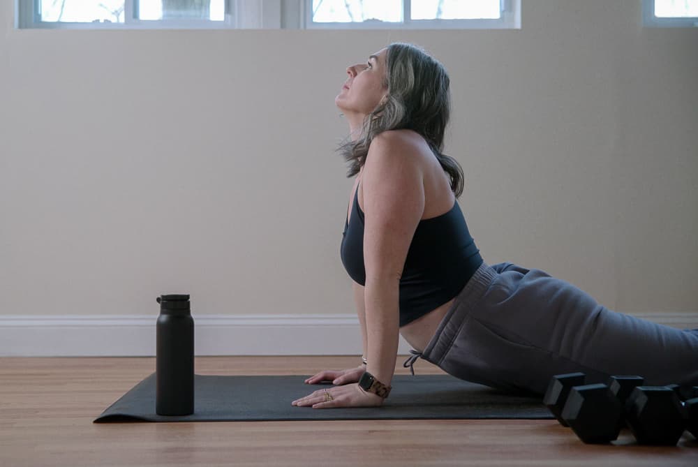 Woman doing a cobra stretch on a mat next to a pair of dumbbells