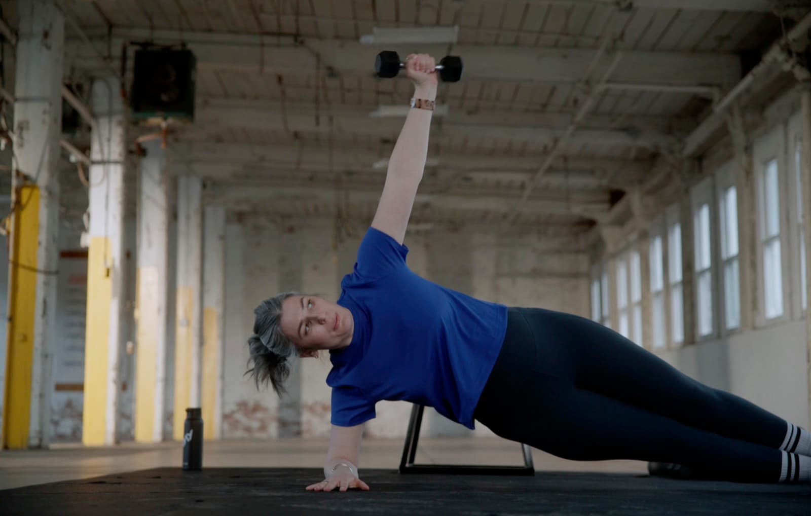 Woman holding a side plank and reaching a light dumbbell toward the ceiling